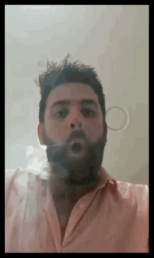 a man with a beard wearing a pink shirt is blowing smoke out of his mouth