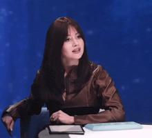 a woman in a brown leather jacket is sitting in front of a blue screen