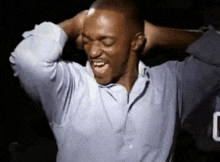 a man in a blue shirt is laughing with his hands behind his head