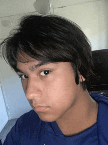 a young man wearing a blue shirt looks at the camera