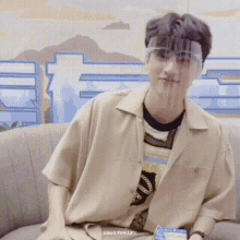a young man is sitting on a couch wearing a face shield and glasses .