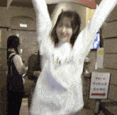 a woman in a white sweatshirt is standing with her arms in the air .
