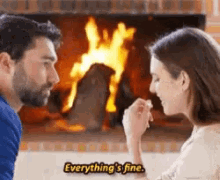 a man and a woman are sitting in front of a fireplace talking to each other .