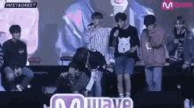 a group of young men are standing on a stage in front of a microphone .