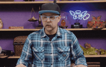 a man wearing glasses and a plaid shirt stands in front of a neon sign that says angel