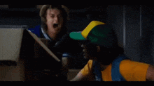 a man in a yellow shirt and blue vest is opening a refrigerator door .
