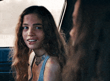 a woman with long hair and a necklace is smiling in a car