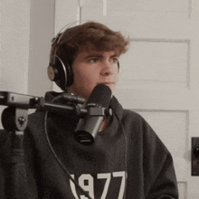 a young man wearing headphones and a 1977 sweatshirt is sitting in front of a microphone .