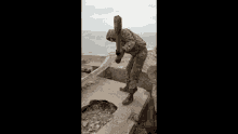 a man in a military uniform is standing on top of a concrete wall holding a hammer .