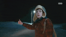 a young boy wearing a plaid jacket and a hat gives a thumbs up sign