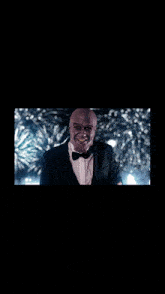 a man in a tuxedo is holding a glass of wine in front of a fireworks display