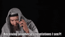 a man in a keffiyeh is holding a cell phone and says receiving prophecies / revelations i see !