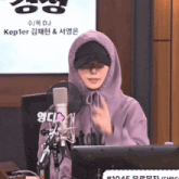 a woman wearing a purple hoodie stands in front of a microphone with the name kepler on the screen