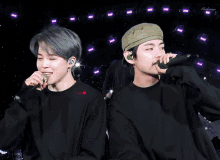 two boys singing into microphones on a stage with purple lights