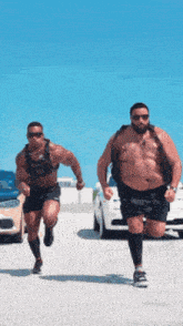two muscular men are running in a parking lot with cars in the background