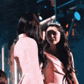 two women are standing next to each other and one has a tiara on her head .
