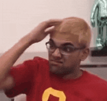 the man is wearing glasses and a red shirt and is scratching his head .