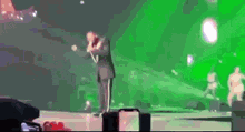 a man in a suit is singing into a microphone on a stage in front of a green background .
