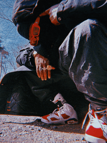 a man wearing sunglasses and a ring sits on the ground with a skateboard in the background