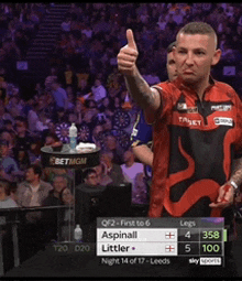 a man giving a thumbs up in front of a scoreboard