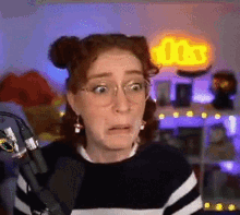 a woman wearing glasses is standing in front of a microphone and making a funny face .