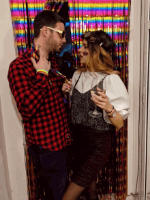 a man and a woman are standing next to each other in front of a rainbow colored curtain