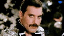 a close up of a man with a mustache wearing a black jacket .