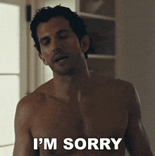 a shirtless man says " i 'm sorry " in front of a window