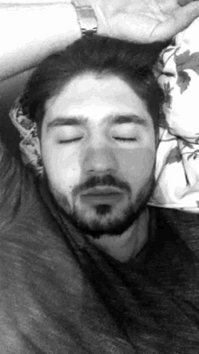 a man with a beard is laying in bed with his eyes closed and his hand on his head .