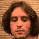 a man with long hair and a beard looks at the camera with his eyes closed