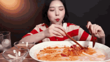a woman is eating noodles with chopsticks from a large white plate