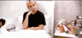 a woman in a black shirt is sitting in a bed with a man sleeping in the background .