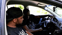 a man wearing a black shirt with the word kill on it sits next to another man in a car