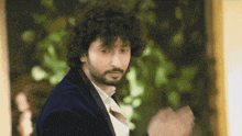 a man with curly hair and a beard wearing a blue jacket and white shirt