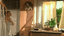 a woman in a white towel is standing in front of a window with a plant on it