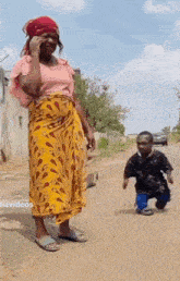 a woman is talking on a cell phone while standing next to a small boy .