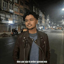 a man in a leather jacket is standing on a street at night