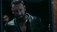 a man in a black leather jacket stands in a dark room with a w logo on the wall
