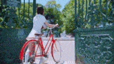 a woman in a white dress is riding a red bicycle through a gate