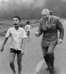 a man in a suit is holding the hand of a young boy who is running down a road .