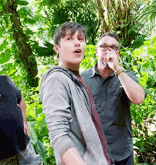 a man with glasses is covering his nose while standing in the woods .