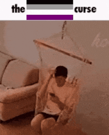 a man is sitting in a hammock in a living room looking at his cell phone .