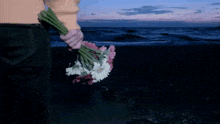 a woman is holding a bouquet of flowers on a beach