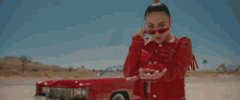 a woman wearing sunglasses and a red jacket stands in front of a red car