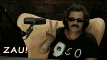 a man wearing headphones and sunglasses is giving a peace sign in front of a microphone with the word zau written in red