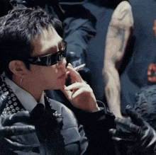 a man wearing sunglasses is smoking a cigarette in a dark room
