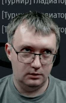 a man wearing glasses and a grey shirt is looking at the camera .