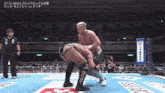 two men are wrestling in a wrestling ring with a referee watching .