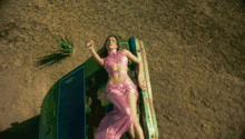 a woman in a pink top and skirt is laying on a green chair in the sand