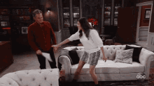 a man and a woman are having a pillow fight in a living room with abc written on the bottom of the screen
